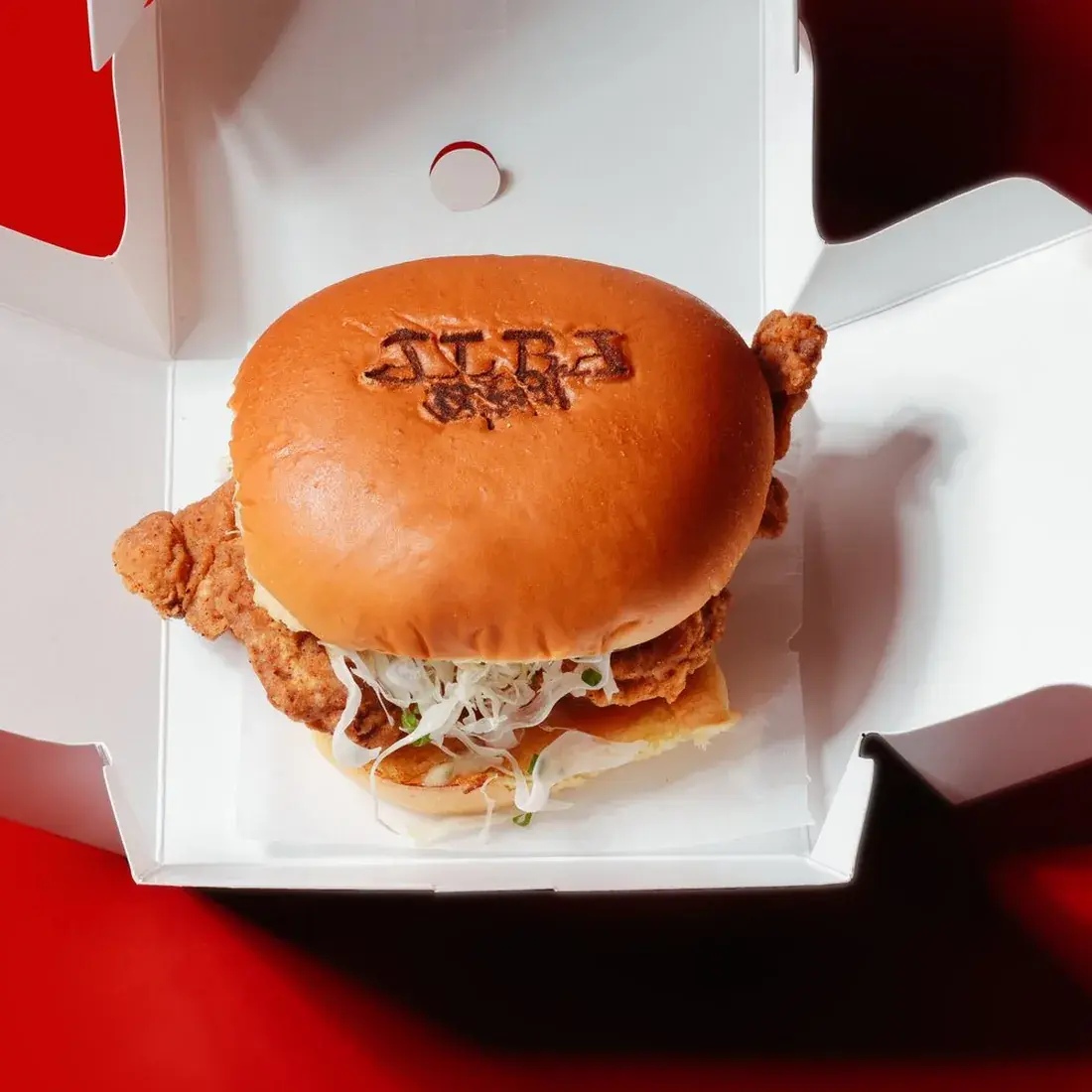 Yuzu Chili Chicken Burger in an Alba Street takeaway box against a red backdrop at Alba Street, Social Distrikt, Dubai Mall